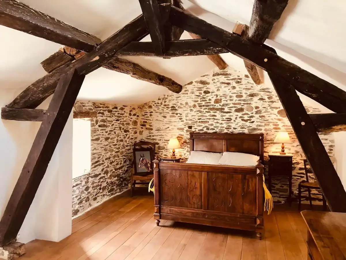 Chambre sous les poutres avec lit ancien en bois et murs en pierre