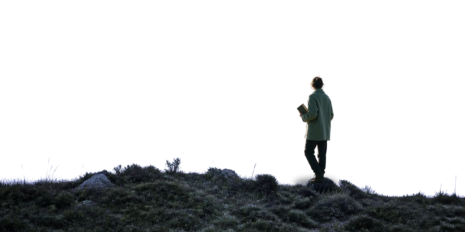 Une personne, un livre à la main, regarde le village depuis les hauteurs de la Montagne Noire.