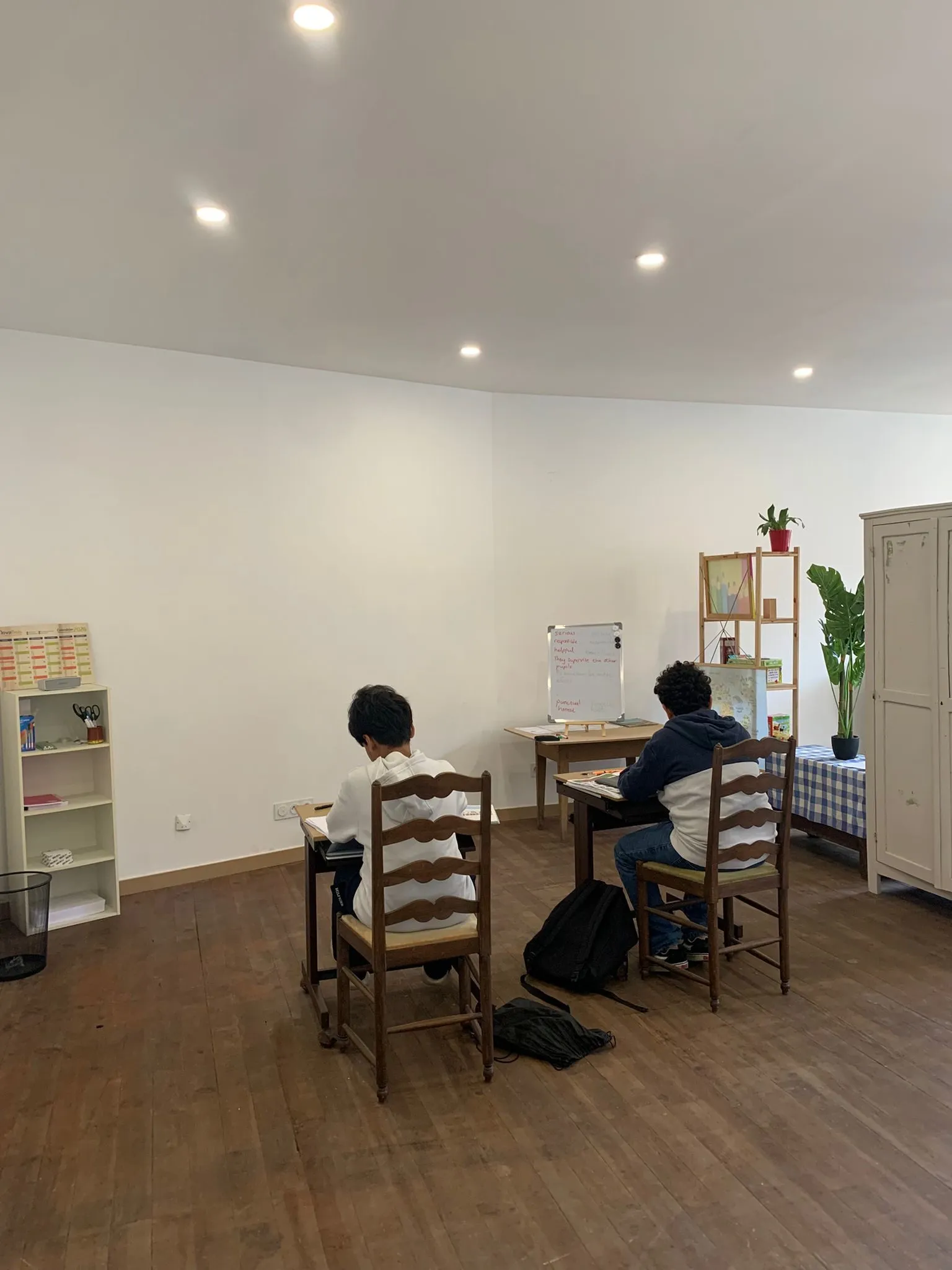 La salle de cours : deux élèves à leur table, la bibliothèque et l’armoire