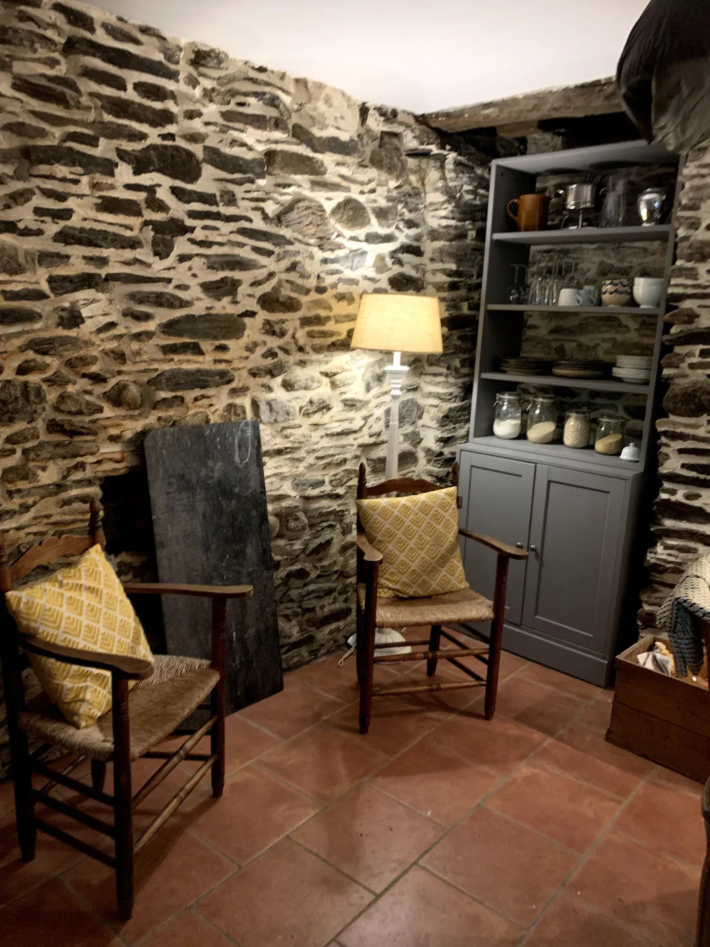 Pièce en pierre apparente avec deux fauteuils paillés et une lampe